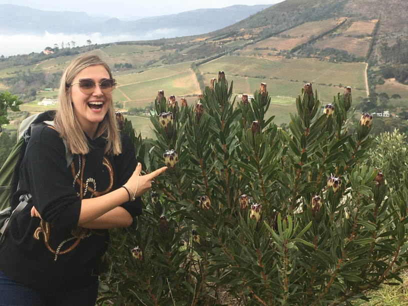 Adele Julier pointing at a flowering bush with a farming landscape in the background. Photo provided by Adele Julier